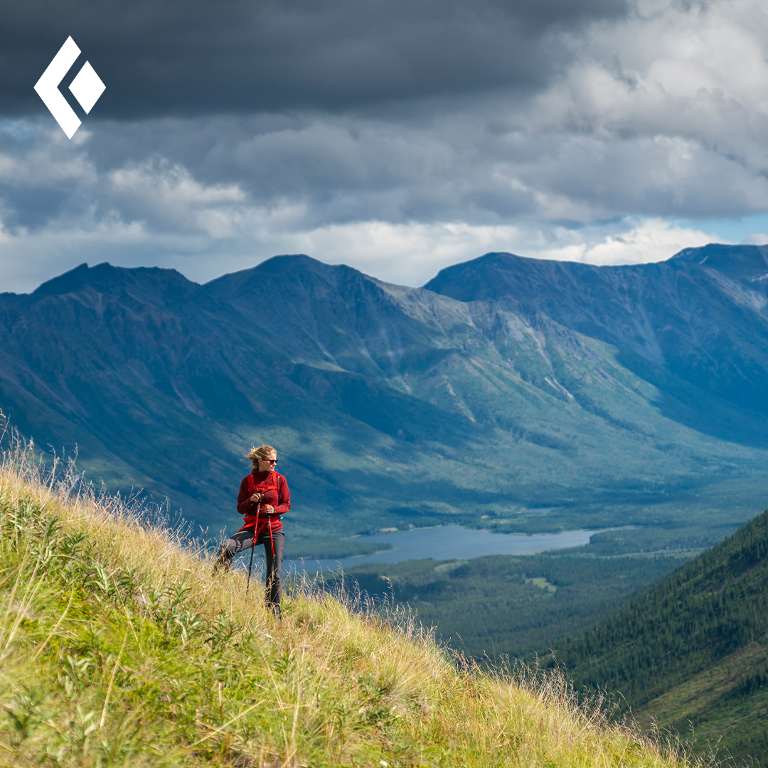 Person on grass hill with mountains in the background